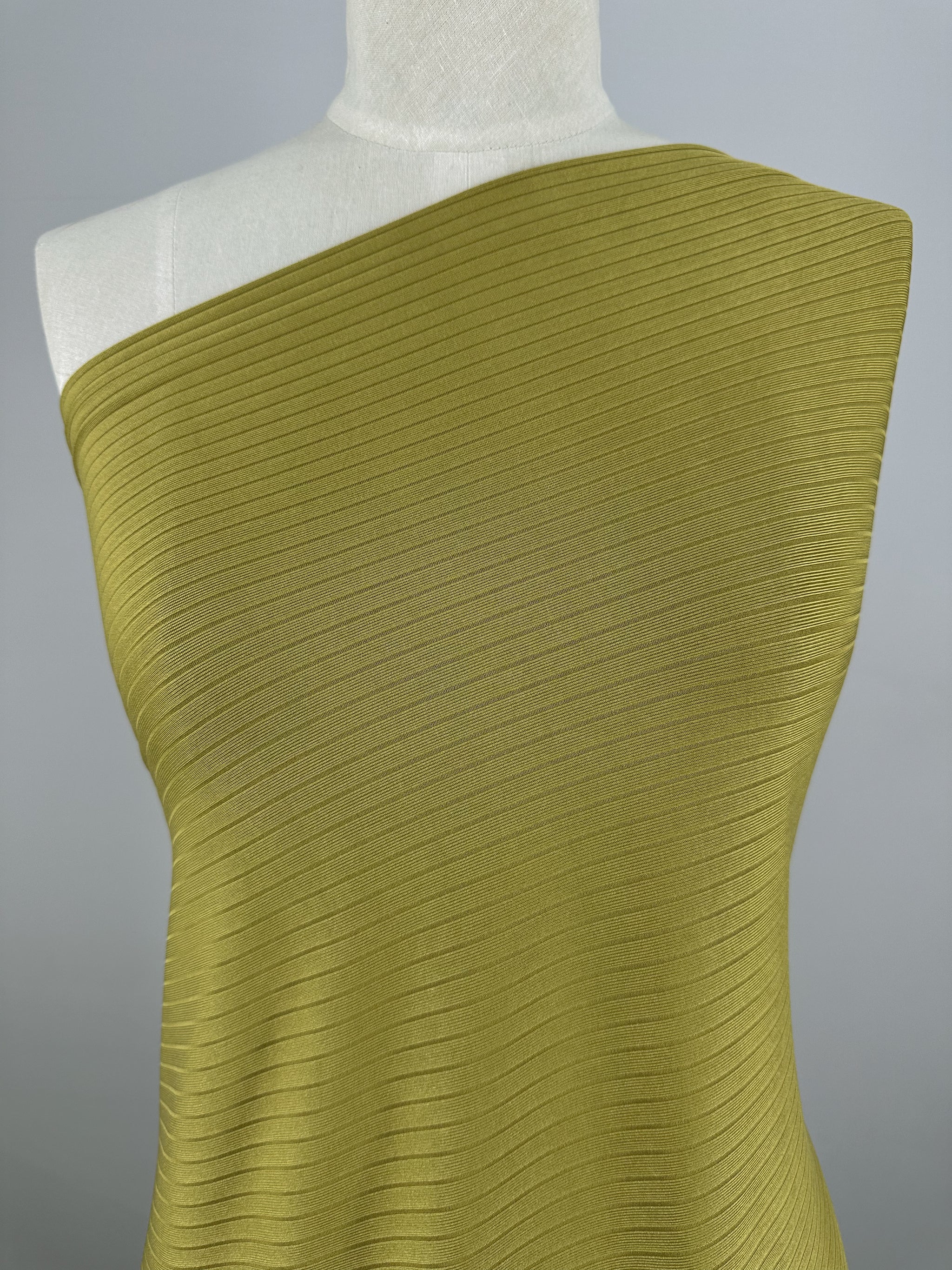 A mannequin is adorned with Super Cheap Fabrics' Rib Knit - Avocado Oil, a 173cm medium weight fabric with diagonal lines. The neutral gray backdrop accentuates its stretchy comfort and texture.