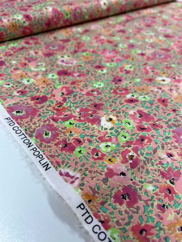 Close-up of a roll of 'Printed Cotton - Poppy Colours - 112cm' by Super Cheap Fabrics, showcasing natural fibers with a delicate design of small, multicolored flowers in pink, green, and orange with white accents. The fabric edges are visible with "PTD COTTON POPLIN" printed along the side.