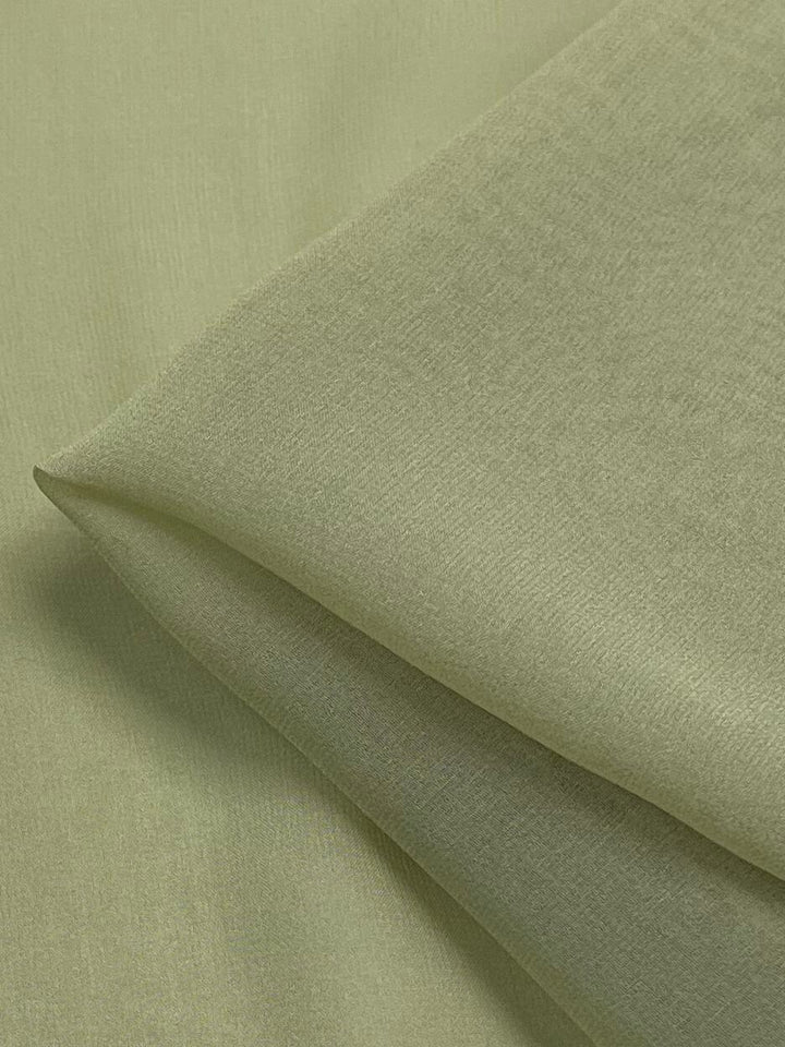 A close-up shot showcases a neatly folded piece of Super Cheap Fabrics' Silk Georgette - Celery, measuring 135cm. The light green fabric boasts a smooth and soft texture, making it perfect for spring and summer outfits. Its surface appears even and consistent in color, with meticulously folded edges highlighting its quality.