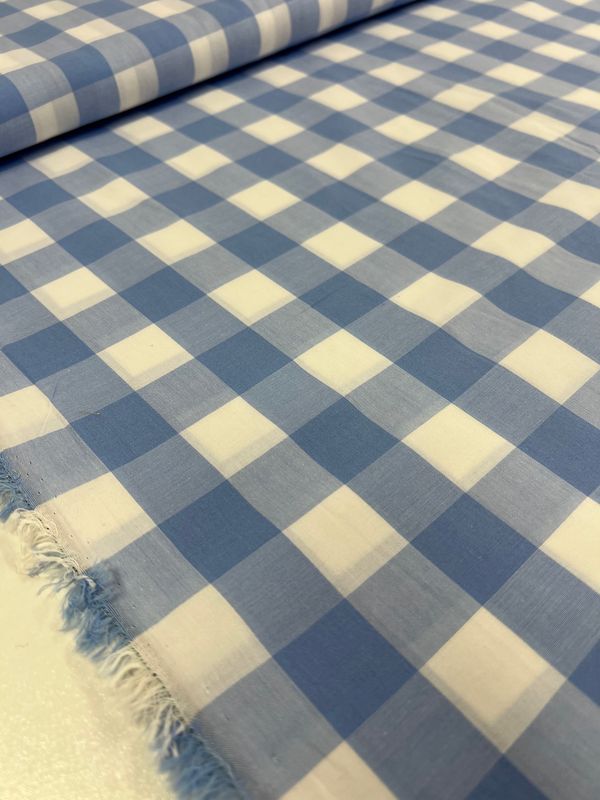 Close-up of the Cotton Gingham XL - Windsurfer by Super Cheap Fabrics, featuring a blue and white checkered pattern with a frayed edge on one side. This lightweight 112cm fabric, rolled out to display its grid design, is crafted from natural cotton fibers and is commonly used for clothing or home decor.