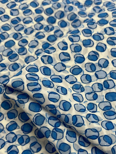 Close-up of Salt Shrunk Print - Cells by Super Cheap Fabrics, featuring a pattern of overlapping blue and white circles. The vibrant 100% Polyester fabric, 155cm wide, has slight wrinkles enhancing the textured design.