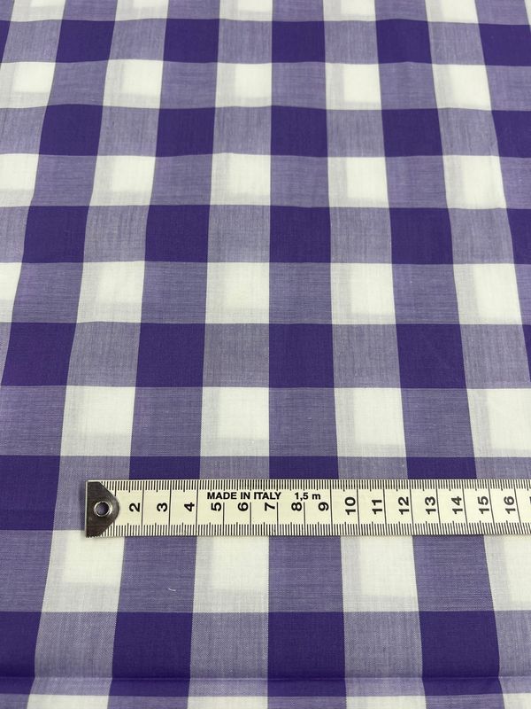 The Cotton Gingham XL - Sand Verbena by Super Cheap Fabrics features blue and white checkered printed cotton fabric. It has a measuring tape placed horizontally across the bottom, indicating measurements in centimeters. Made from natural cotton fibers, this versatile 112cm-wide material is ideal for various applications.