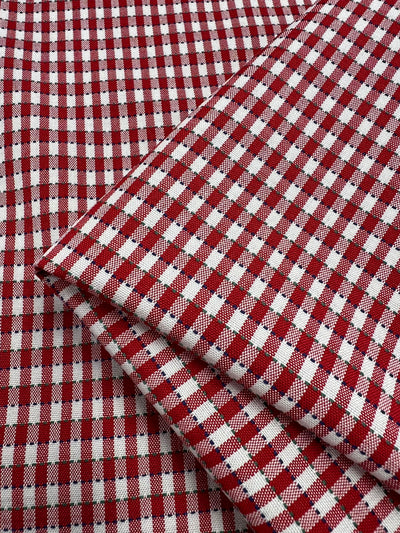 A close-up of Super Cheap Fabrics' Shirting - Riding fabric, featuring a classic red and white gingham crisscross pattern. This neatly folded, lightweight fabric measures 145cm wide and is perfect for creating timeless designs.