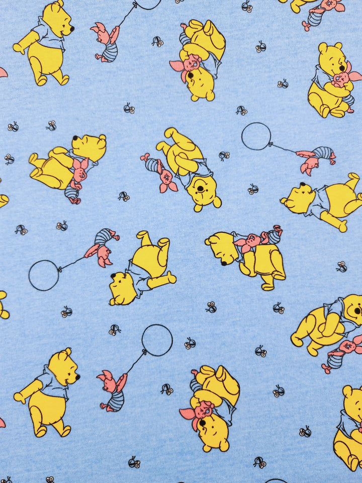 The Printed Jersey - Winnie & Co by Super Cheap Fabrics features a light blue poly/cotton blend with cartoon yellow bears in blue shirts and pink pigs holding balloons. Small bees add charm to this whimsical, lycra-enhanced 170cm fabric design.