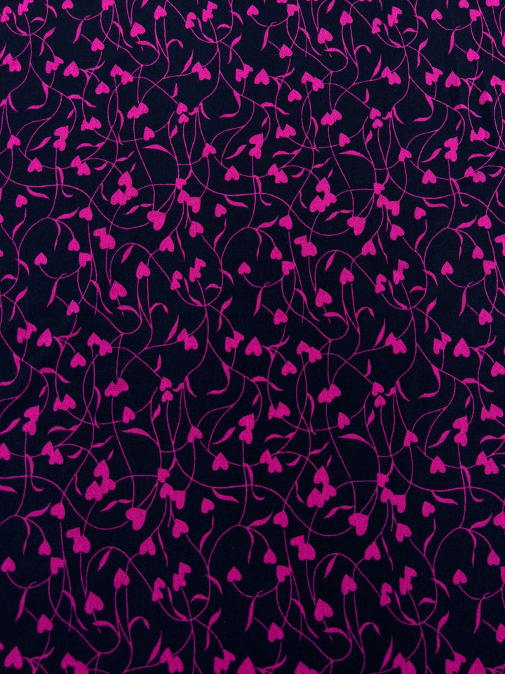 A close-up view of the Super Cheap Fabrics' Printed Lycra - Barbwire Heart - 150cm displaying an intricate pattern of navy pink vines and heart-shaped leaves on a dark purple background. The design creates a sense of movement and elegance.