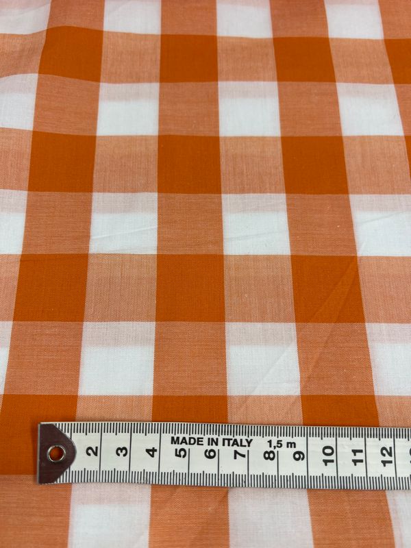 A close-up of the Cotton Gingham XL – Orange – 112cm by Super Cheap Fabrics, showcasing a measuring tape at the bottom with measurements in centimeters. Made from natural cotton fibers, this fabric is labeled "Made in Italy" and is ideal for elegant home decor projects.