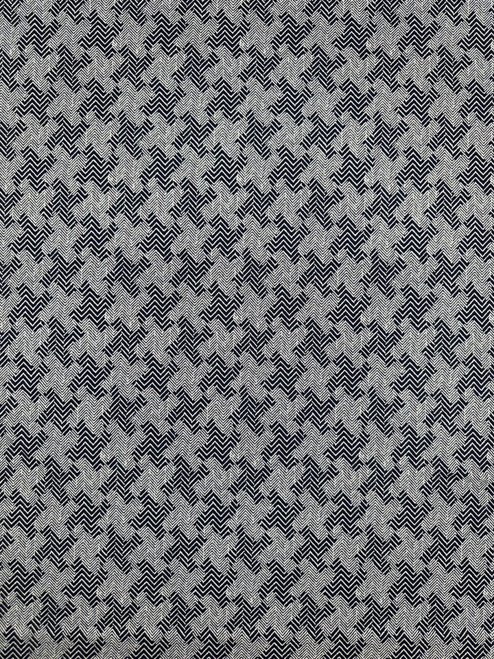 The "Printed Lycra - Tazo - 150cm" fabric from Super Cheap Fabrics features a medium-weight gray material adorned with a geometric houndstooth pattern in black. This pattern consists of a repetitive arrangement of jagged lines and angular shapes, offering a detailed texture. Made from Polyester/Spandex, the fabric showcases an intricate, eye-catching design.