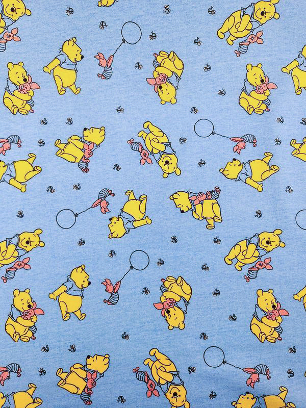 The Super Cheap Fabrics' Printed Jersey - Winnie & Co features cartoon characters, such as a yellow bear and a pig with balloons and bees, set on a light blue backdrop. Width: 170cm.