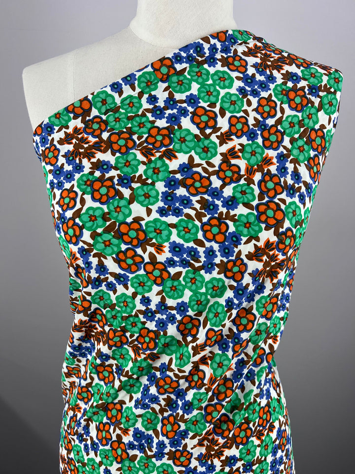 A mannequin showcases Super Cheap Fabrics' Salt Shrunk Print - Kaleid, 155cm. The vibrant fabric features a floral pattern with green, orange, red, and blue flowers on a white background, elegantly displaying its colorful and lively design.