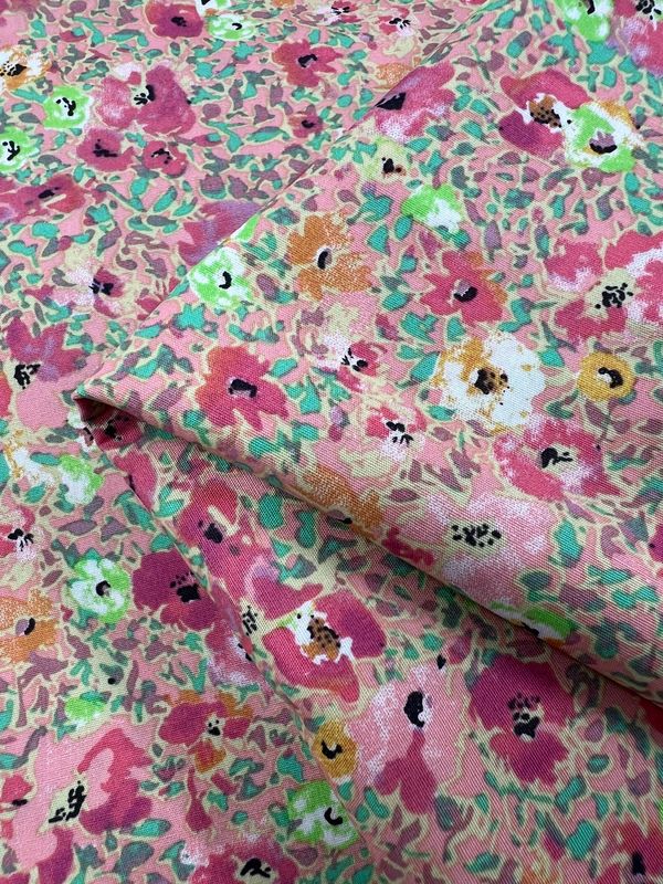 A close-up of the "Printed Cotton - Poppy Colours - 112cm" by Super Cheap Fabrics reveals a vibrant floral pattern in pink, green, white, and yellow. The natural fibers are elegantly folded, highlighting colorful abstract flowers in this printed cotton masterpiece.