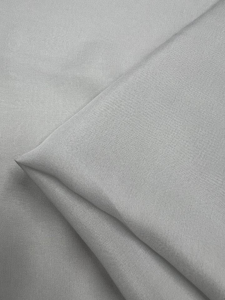 A close-up image of the Pure Silk Chiffon in Silver by Super Cheap Fabrics, neatly folded with a smooth texture. The 100% silk material's subtle sheen and finely woven nature are visible, highlighting its soft and elegant appearance at 140cm in width.