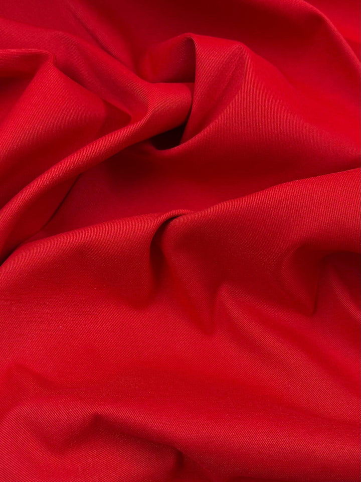 A close-up image of vibrant Delustered Satin - Goji Berry - 150cm fabric from Super Cheap Fabrics with folds and creases, creating a textured, wavy surface. The 100% polyester material appears smooth and slightly glossy, highlighting the rich, solid color.