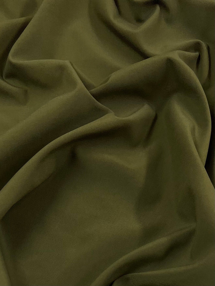 Close-up of dark green fabric with folds and wrinkles, creating a textured and wavy surface. The material appears soft and smooth, draping naturally like Delustered Satin - Olive Drab - 150cm by Super Cheap Fabrics.