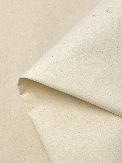 A close-up of a piece of **Super Cheap Fabrics' Calico - 125cm** fabric with a subtle texture, possibly made of cotton or linen. The undyed fabric is folded neatly in one corner, showcasing its smooth surface and light, natural color with tiny speckled details, reminiscent of calico used in mockup garments.