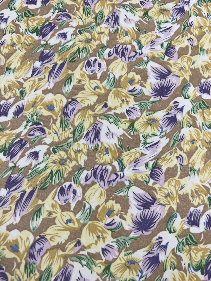 The Printed Georgette - Earths Bloom - 150cm from Super Cheap Fabrics features a dense, intricate floral pattern with yellow, white, and purple flowers interspersed with green leaves on a brown background. The sheer polyester design beautifully covers the entire visible surface.