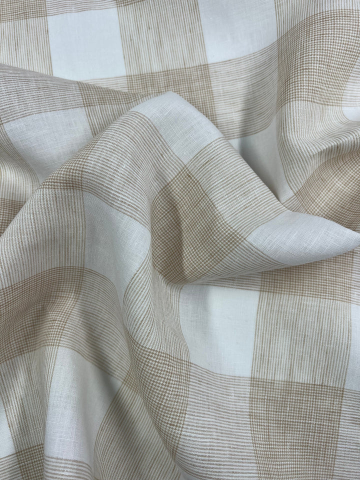 A close-up image of a beige and white checkered fabric with a soft, crinkled texture. The 100% linen fabric, Pure Linen - Natural Check - 145cm by Super Cheap Fabrics, features alternating square patterns with fine lines and solid sections, creating a subtle and elegant design. The material is lightweight, perfect for making outfits that are slightly translucent.