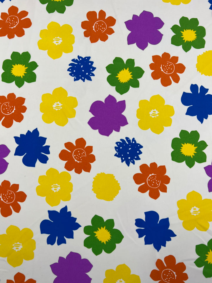 A vibrant pattern featuring colorful flowers scattered randomly on a white background. The bright prints in shades of red, orange, yellow, green, blue, and purple have distinct shapes and petal designs. Made from durable polyester fabric, the Deluxe Print - Flower Spread - 150cm by Super Cheap Fabrics creates a lively and cheerful appearance perfect for designer fabrics.