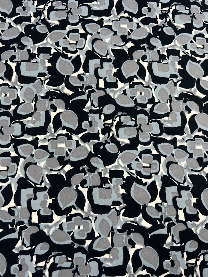 A close-up view of a Deluxe Print - Flower Blocks - 150cm by Super Cheap Fabrics with an abstract pattern consisting of interconnected shapes. The design features shades of gray and black with a few white accents. The shapes appear to be a mix of geometric and organic forms, creating a complex, dense pattern.