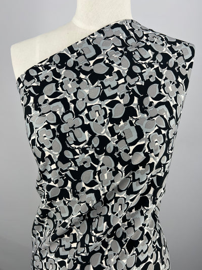 Mannequin draped in a Deluxe Print - Flower Blocks - 150cm fabric by Super Cheap Fabrics, featuring abstract floral shapes. The easy care fabric cascades smoothly over the mannequin, showcasing its texture and design. The background is plain and neutral, highlighting the intricate details of the versatile fabric.