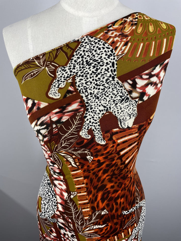 A close-up of a mannequin draped in vibrant, animal-print Printed Lycra - Geo Panther - 147cm by Super Cheap Fabrics. The design features a mix of leopard and cheetah patterns, with prominent depictions of large cats and abstract geometric shapes in shades of brown, green, and white.