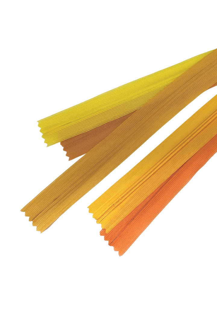 A group of Invisible Zip - 30cm in Yellows & Oranges, from Super Cheap Fabrics, is arranged diagonally, showcasing various shades of yellow and orange. Known for their durable teeth, the zippers are displayed against a white background. The vibrant colors create a visually appealing and organized pattern with an elegant finish.