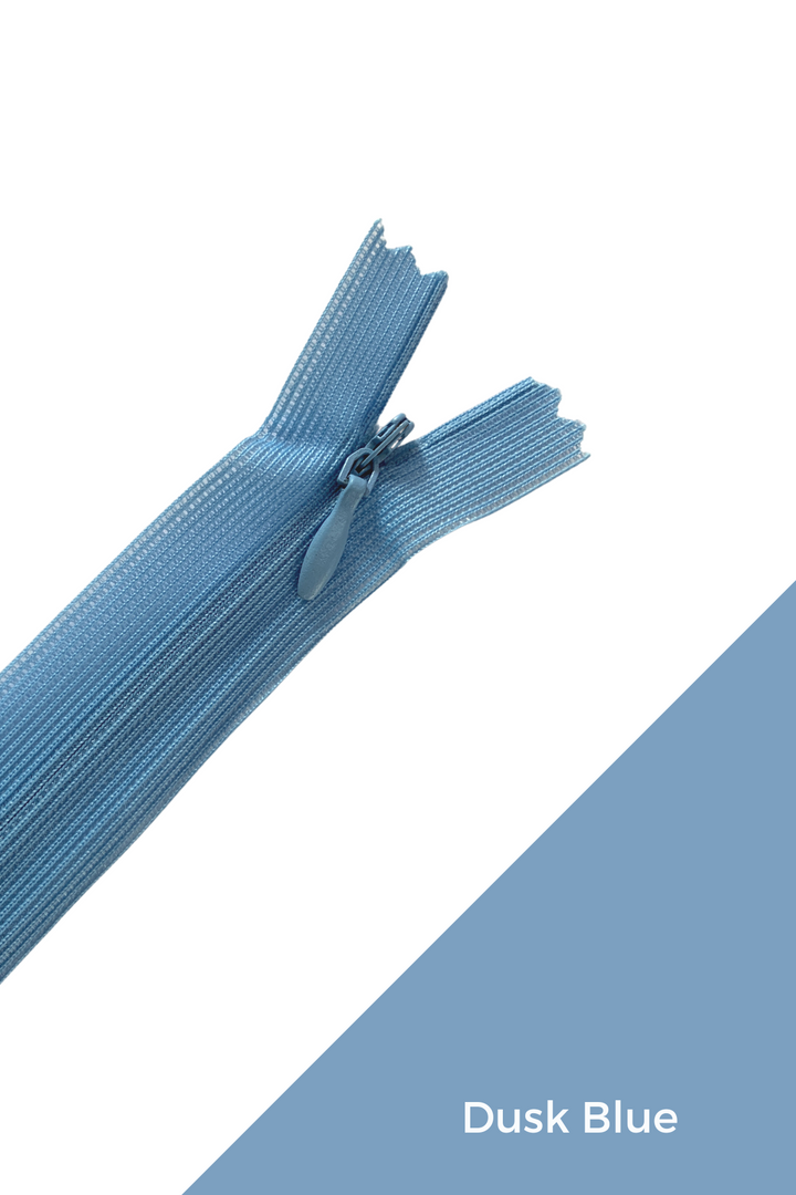 A close-up of an elegant Invisible Zip - 30cm - Blues from Super Cheap Fabrics in dusk blue on a white and dusk blue background. The 100% polyester zipper is partially open, revealing the slider and teeth. "Dusk Blue" is written in white text on the blue section of the background.