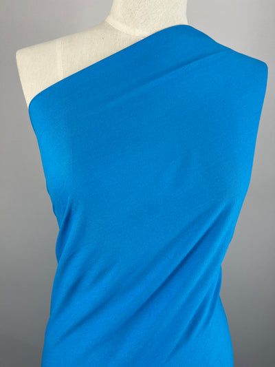 A mannequin showcases the Super Cheap Fabrics' Plain Rayon - Blue Jewel - 140cm, styled in a one-shoulder design against a neutral gray backdrop.