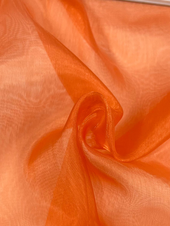 Close-up of Super Cheap Fabrics' Organza - Carrot - 150cm, featuring a vibrant orange color, soft folds, and a subtle sheen that gives it a textured and flowing appearance.